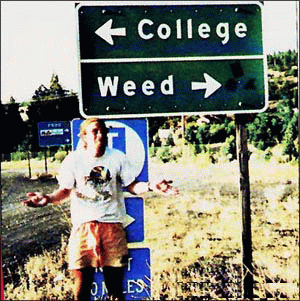 Red headed 20y/o man with arms spread, standing under road sign showing <--College or Weed-->